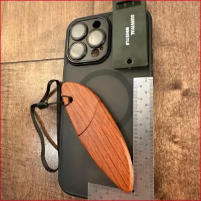 Black iPhone 14 case with survival whistle, frame ruler, wooden USB drive, and box opener