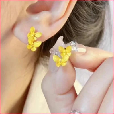 Delicate yellow double butterfly stud earrings held near an ear for secure shipping