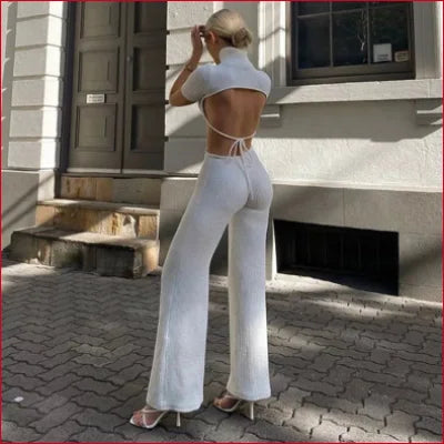 Woman in a white turtleneck cutout knitted jumpsuit with wide-leg pants and heels