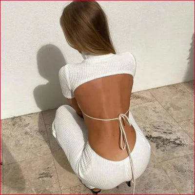 Backless white turtleneck cutout knitted dress worn by a woman sitting on the floor