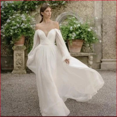 Elegant off-shoulder white chiffon beach wedding dress with long sleeves and flowing skirt