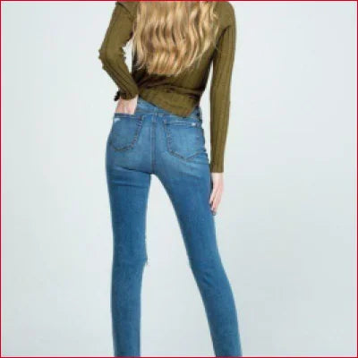 Pair of destroyed skinny denim jeans with clean hem worn by person in green top