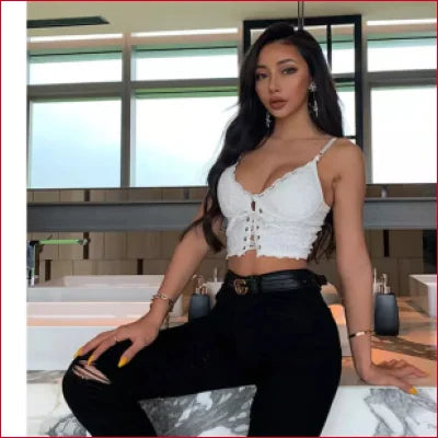 Woman in white lace strap crop top and black pants posing for club wear fashion