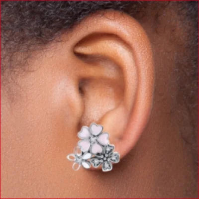 Floral-shaped sterling silver stud earrings resembling pink daisies worn on earlobe