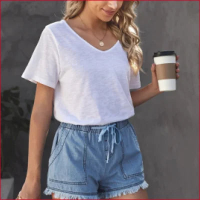 Woman in casual denim shorts holding a coffee cup, styled with a white t-shirt