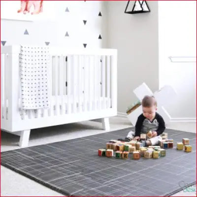 White baby crib next to Premium Stylish Foam Play Mat in large black linen design