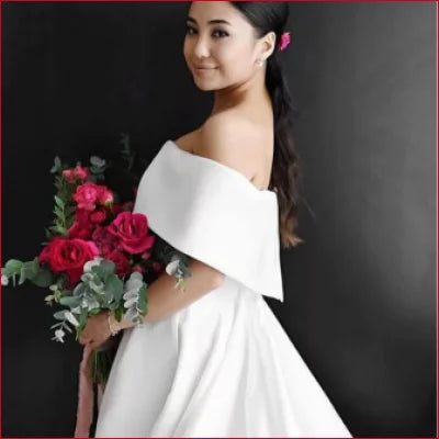 Woman in elegant white off-shoulder bridal gown holding red rose bouquet