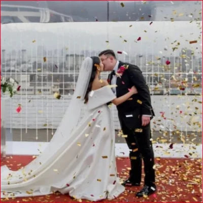 Newlywed couple kissing in Elegant Satin Off Shoulder Bridal Gown with confetti and petals