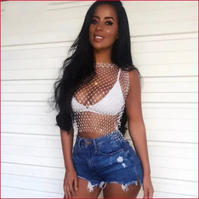 Woman in sheer fishnet top with rhinestones, styled for summer in denim shorts