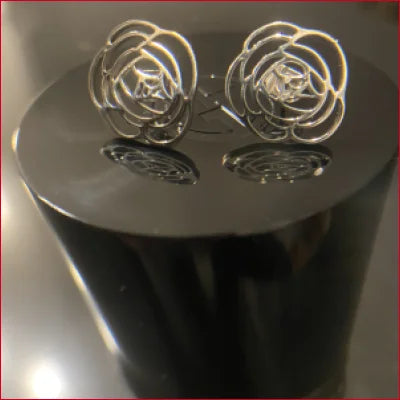 Pair of silver rose-shaped stainless steel stud earrings on a reflective surface