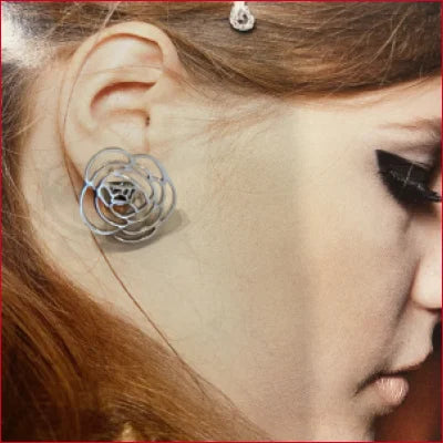 Delicate silver rose-shaped stainless steel stud earrings worn on an ear