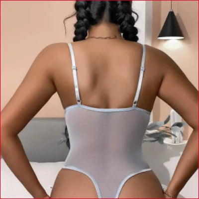 Light gray embroidered thong bodysuit with lace details, worn by a person with dark curly hair