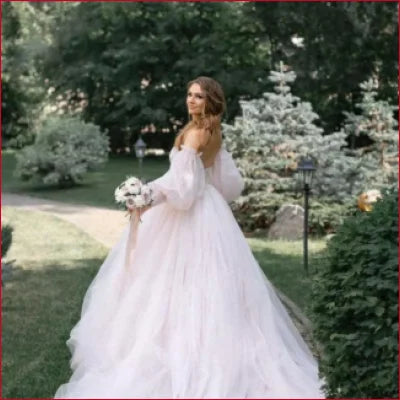 Bride in a flowing white wedding gown with detachable puffy sleeves holding a bouquet